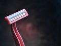 A pink razor for depilation against a dark concrete wall