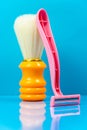 Pink razor stands with an orange shaving brush on a blue background