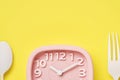 Pink retro alarm clock and white spoon and fork on yellow background with copy space. Time concept