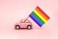 Pink retro toy car delivering bright rainbow gay flag on the soft pink backgraund. Concept of gay parade, LGBT community, adoption Royalty Free Stock Photo