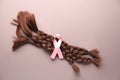 Braided strands and pink ribbon on color background. Concept of hair donation for breast cancer patients