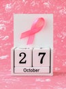 Pink ribbon of breast cancer awareness on a white wooden perpetual calendar with date 27 october. International breast cancer