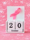 Pink ribbon of breast cancer awareness on a white wooden perpetual calendar with date 20 october. International breast cancer