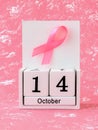 Pink ribbon of breast cancer awareness on a white wooden perpetual calendar with date 14 october. International breast cancer