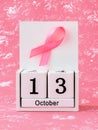 Pink ribbon of breast cancer awareness on a white wooden perpetual calendar with date 13 october. International breast cancer