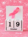 Pink ribbon of breast cancer awareness on a white wooden perpetual calendar with date 19 october. International breast cancer