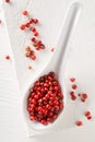 Pink or rose brazilian red peppercorns schinus terebinthifolius in white spoon on rustic white wooden table background Royalty Free Stock Photo