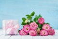 Pink rose flower bouquet and gift box with ribbon on blue table. Greeting card for Birthday, Woman or Mothers Day. Pastel color. Royalty Free Stock Photo