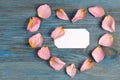 Pink rose petals imaging heart shape on blue wooden board with blank white card inside Royalty Free Stock Photo