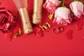 Pink roses flowers, wedding rings, champagne, gift, golden ribbons and confetti hearts on red background. Top view with space for Royalty Free Stock Photo