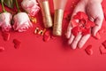 Pink roses flowers, wedding rings in male hands, champagne, gift, golden ribbons and confetti hearts on red background. Top view. Royalty Free Stock Photo