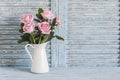 Pink roses in white enamel jug on a blue rustic background. Free space for text.