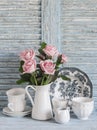 Pink roses in a white enameled pitcher, vintage crockery on blue wooden rustic background. Kitchen still life in vintage style Royalty Free Stock Photo