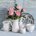 Pink roses in a white enameled pitcher, vintage crockery on blue wooden rustic background. Kitchen still life in vintage style. Royalty Free Stock Photo