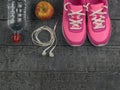 Beautiful pink sneakers, headphones, water and apples on a wooden black floor. View from above. Royalty Free Stock Photo