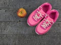 Pink running shoes for fitness classes at the gym and a ripe Apple on a wooden floor. Royalty Free Stock Photo