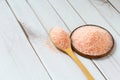 Fine pink Himalayan salt in wooden spoon on a white wooden background