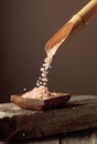 Pink salt is poured with a wooden spoon in the wooden dish Royalty Free Stock Photo