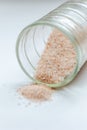 pink salt spill from small glass container on white background