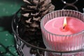 pink scented candle glowing on a mirror tray next to pine cone. christmas fragrance, home decor for holiday.