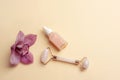 Pink serum bottle, rose quartz crystal facial roller and orchid flower on beige background. Top view, flat lay, copy