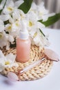 Pink serum bottle and rose quartz facial roller with big white flowers. Beauty, spa and wellness concept. Closeup