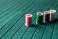 Pink sewing thread with other colorful threads on the green textile background - Image