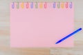 The pink sheet of paper pinned with colored paper clips on the light oak wooden table, with ballpoint pen, for background Royalty Free Stock Photo