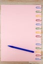 The pink sheet of paper pinned with colored paper clips on the oak wooden table, ballpoint pen, close, for background Royalty Free Stock Photo