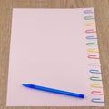 The pink sheet of paper pinned with colored paper clips on the oak wooden table, close, perspective, ballpoint pen, for background Royalty Free Stock Photo