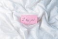 A pink sheet of paper with the words `I love you` on white crumpled fabric