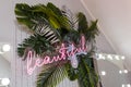 Pink shining neon inscription Beautiful on artificial tropic plant leaves, room interior decoration, lights bokeh, mirror Royalty Free Stock Photo