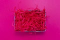 Pink shredded paper packaging material in box flat lay on pink background