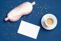Pink sleeping mask, coffee cup and blank paper note on dark classic blue background with confetti. Happy morning, early wake up,