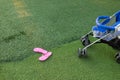 Pink slipper and part of baby stroller on green grass