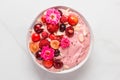 Pink smoothie bowl or nice cream with fresh berries, rose flowers, nuts and seeds on white marble table