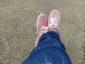 Pink sneakers with white laces on the legs. Blue jeans wrapped underneath. View from above. Carefree and sporty. Crossed legs with