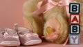 Pink soother falling besides baby shoes blocks and teddy bear