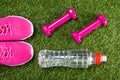Pink sport sneakers and dumbbells for fitness, and a bottle of water against the background of grass Royalty Free Stock Photo