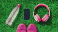 Pink sports sneakers, wireless headphones, blank copy space screen smartphone and plastic bottle of water on green grass