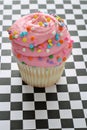 Pink sprinkle cupcake on checkered background