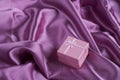 Pink squared gift box on purple satin fabric folds Royalty Free Stock Photo