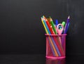 pink stationery glass with multi-colored wooden pencils and pens black chalkboard background