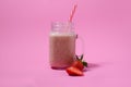 Pink strawberry smoothie in a mason jar glass with straw and scattered berries on pink background. Royalty Free Stock Photo