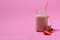 Pink strawberry smoothie in a mason jar glass with straw and scattered berries on pink background. Royalty Free Stock Photo
