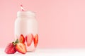 Pink strawberry smoothie with piece juicy fruit in retro jar with red striped straw on light soft pastel pink wall and white wood.