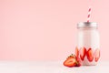 Pink strawberry smoothie with piece juicy fruit in retro jar with red striped straw on light soft pastel pink wall and white wood.