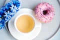 Pink sugar glazed donut, cup of tea and purple hyacinth flower on colorful background. Royalty Free Stock Photo