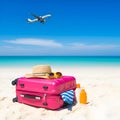 A pink suitcase and hat on the beach with an airplane flying in the background under a clear blue sky Royalty Free Stock Photo