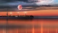 Pink sunset  on pier at sea on horizin promenade with blurred night light cloudy dramatic  blue sky and full big moon on starry sk Royalty Free Stock Photo